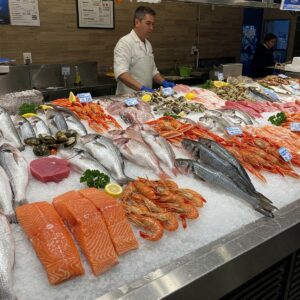 A male customer in a blue shirt looking at the fresh seafood selection at a well-stocked counter, with an employee standing behind it.