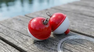 Two traditional red and white plastic round bobbers resting on weathered wooden dock planks, showing the spring-loaded metal clip mechanism.