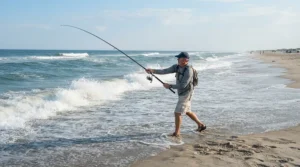 A surf caster wearing durable fishing shorts for hot weather casting a line into ocean surf waves.