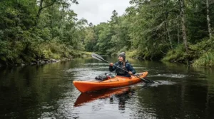 A paddler wearing quick dry fishing shirts for travel navigating a calm river in a red kayak.
