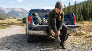 Fisherman putting on hip waders for bank fishing quickly beside a pickup truck tailgate.