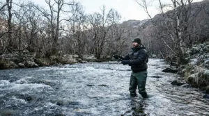 An angler demonstrating cold water wading gear performance in deep, rushing river channels using neoprene waders for cold water fishing.