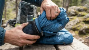 Hands stuffing a packable rain jacket for fishing trips into its own integrated storage pouch.